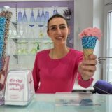 Melissa Favaretto hält eine traditionelle Eiswaffel mit türkisen Farbtupfern und einer Kugel Erdbeereis in die Kamera.