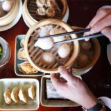 Ein Mann greift in einem chinesischen Restaurant mit Essstäbchen nach Dim sum, gedämpfte Teigtaschen, die in einem Bambuskorb liegen.