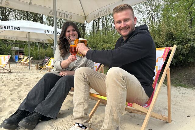 Eine Frau und ein Mann sitzen auf Strandstühlen und stoßen mit Getränken an