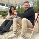 Eine Frau und ein Mann sitzen auf Strandstühlen und stoßen mit Getränken an