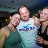 Zwei Frauen und ein Mann stehen auf einer Tanzfläche und lächeln in die Kamera.