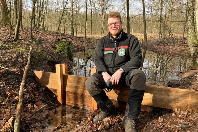 RVR-Förster Frederik Vollmer sitzt im Naturschutzgebiet Brinksknapp auf einem kleinen Wehr, mit dem Wasser gestaut wird.