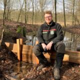RVR-Förster Frederik Vollmer sitzt im Naturschutzgebiet Brinksknapp auf einem kleinen Wehr, mit dem Wasser gestaut wird.