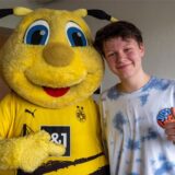 Das BVB-Maskottchen Emma umarmt eine Patientin.