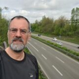 Ein Mann steht auf einer Autobahnbrücke und schaut in die Kamera.