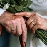 Hände eines alten Ehepaares. Der Mann trägt den Ehering an der rechten, die Frau an der linken Hand.