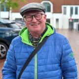 Ein Mann mit Brille und Mütze lächelt fröhlich in die Kamera.