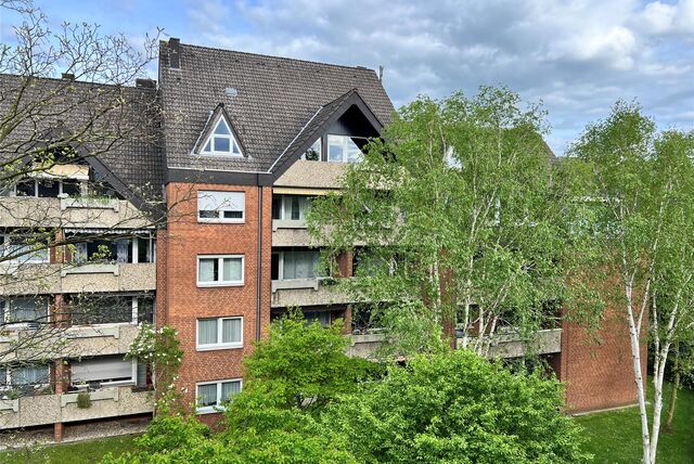 Ein Wohnungshaus von außen. Davor stehen Bäume.