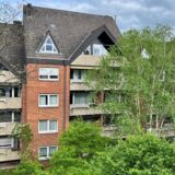 Ein Wohnungshaus von außen. Davor stehen Bäume.