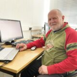 Klaus Martin, der mit dem Hertener Bürgerpreis ausgezeichnet worden ist, sitzt in seinem Rollstuhl an einem Tisch, auf dem ein Laptop steht sowie ein weiterer Bildschirm samt Tastatur.