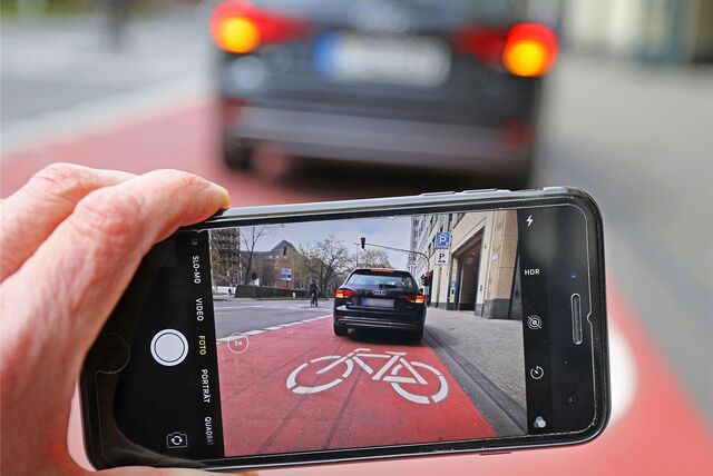 Ein Handy fotografiert einen Falschparker, der verbotenerweise auf dem Radweg hält.