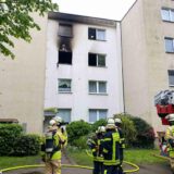 Feuerwehrleute stehen vor einem Haus in Gladbeck mit Rauchspuren an einem Fenster im dritten Obergeschoss.