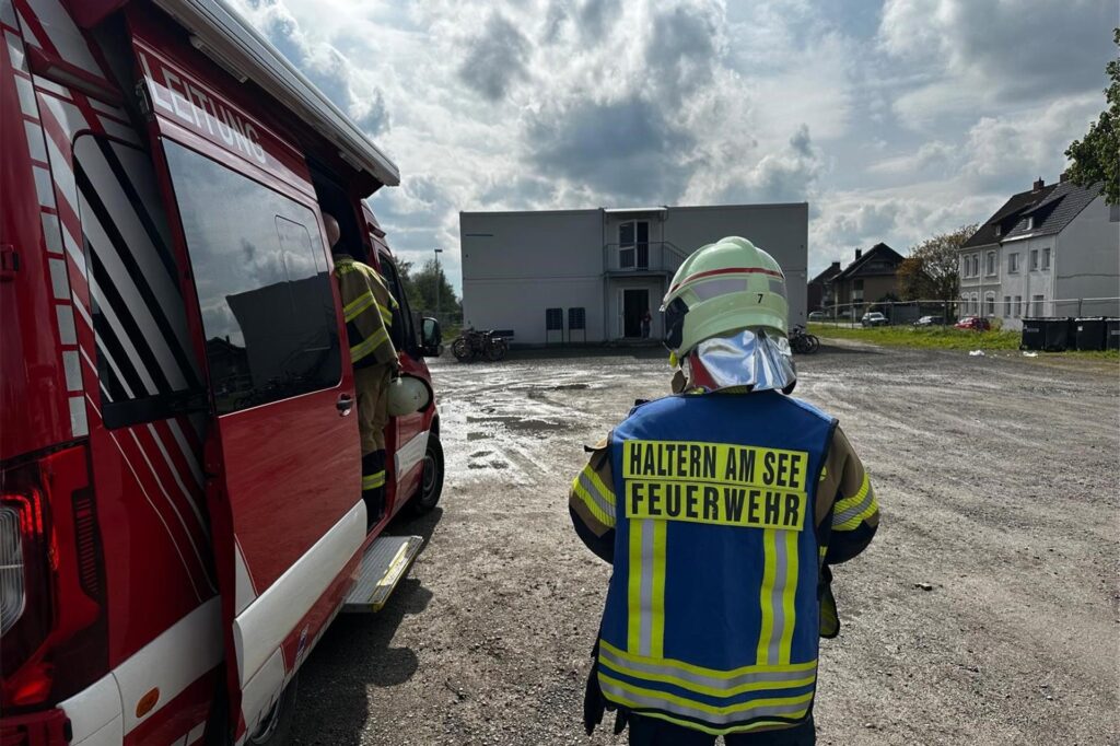 Feuerwehrmann steht neben Feuerwehrwagen an der Flüchtlingsunterkunft