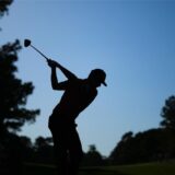 Ein Mann im Gegenlicht hat einen Golfschläger in der Hand und holt zum Schlag aus.