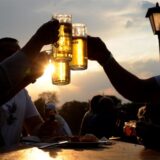 Drei Menschen stoßen in der Dämmerung mit Bier an. Die Sonne scheint in die Gläser und lässt das Bier golden schimmern.