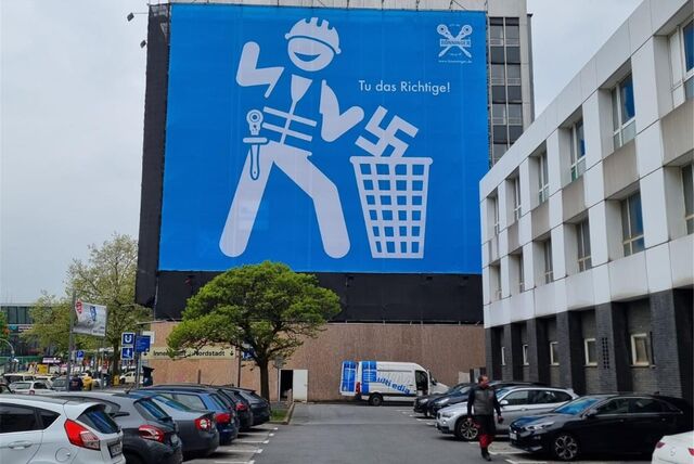 Am Dortmunder Hauptbahnhof hängt ein großes Plakat. Darauf zu sehen ist ein stilisierter Handwerker, der ein Hakenkreuz in einen Mülleimer schmeißt.