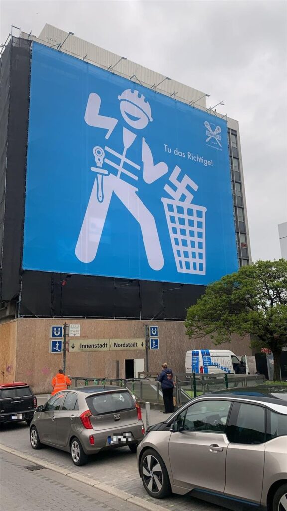 Am Dortmunder Hauptbahnhof hängt ein großes Plakat. Darauf zu sehen ist ein stilisierter Handwerker, der ein Hakenkreuz in einen Mülleimer schmeißt. Am Dortmunder Hauptbahnhof hängt ein großes Plakat. Darauf zu sehen ist ein stilisierter Handwerker, der ein Hakenkreuz in einen Mülleimer schmeißt.