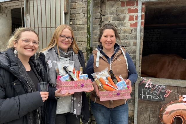 Drei Frauen mit Geschenken in der Hand. Sie stehen vor einer Pferdebox.