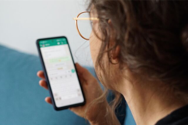 Eine junge Frau hält ihr Smartphone in der Hand und liest eine Whatsapp-Nachricht.