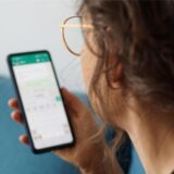 Eine junge Frau hält ihr Smartphone in der Hand und liest eine Whatsapp-Nachricht.
