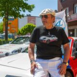 Ein Mann mit Sonnebrille lehnt an der Motorhaube eines Sportwagens.