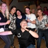Der Sänger der Band Take 5 kniet vor einer Gruppe von fünf feiernden Frauen und sind in ein Mikrofon.