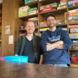 Jerome Wenzel (r.) und Marvin Kübber stehen vor einer rustikalen Regalwand mit vielen Gesellschaftsspielen.
