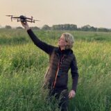 Carolin Beforth hält eine Drohne in der Hand, während sie auf einer Wiese steht.