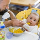 Ein Vater füttert seinen acht Monate alten Sohn mit Brei.