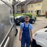 Der Hertener Egzon steht neben seinem Transport, mit dem er nicht problemlos auf sein Grundstück im Hintergrund des Bildes fahren kann. Grund dafür sind zwei Autos, die hinter und neben ihm abgestellt sind.
