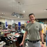 Jens Grosse-Kreul steht lächelnd in seinem Schuhgeschäft. Im Hintergrund sind Schuhe und Kleidung zu sehen.