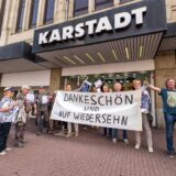 Das Karstadt-Gebäude auf dem Altstadtmarkt in Recklinghausen von außen betrachtet. Eine Menschengruppe steht mit einem Transparent davor.
