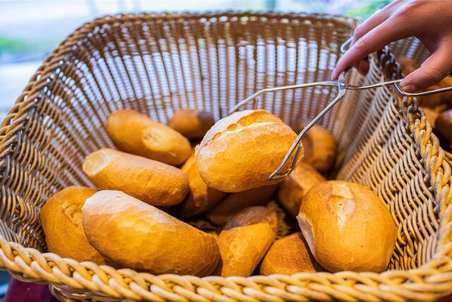 Eine Bäckerei-Verkäuferin nimmt ein Brötchen mit einer Zange aus einem Brötchenkorb.