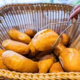 Eine Bäckerei-Verkäuferin nimmt ein Brötchen mit einer Zange aus einem Brötchenkorb.