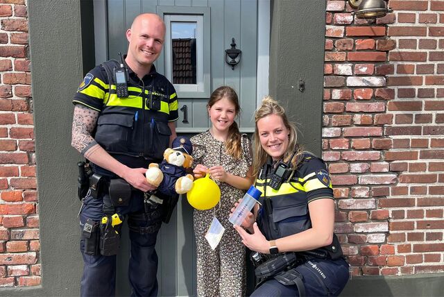 Beamte von der Polizei Nederweert stehen neben einem Mädchen, das seinen gelben Luftballon in der Hand hält.