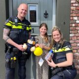 Beamte von der Polizei Nederweert stehen neben einem Mädchen, das seinen gelben Luftballon in der Hand hält.