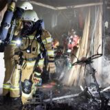 Feuerwehrleute stehen vor einer Garage und dem verkohlten Wrack eines E-Scooters.
