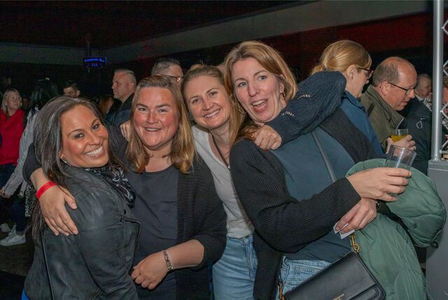 Vier Frauen stehen nebeneinander auf einer Party und halten sich lachend im Arm.