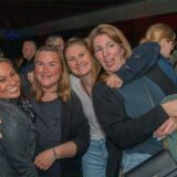 Vier Frauen stehen nebeneinander auf einer Party und halten sich lachend im Arm.