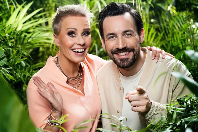 Sonja Zietlow und Jan Köppen, Moderatoren des Dschungelcamps, stehen zwischen mehreren Pflanzen.