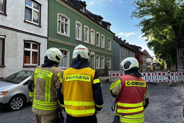 Drei Feuerwehrmänner stehen auf einer Straße.