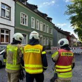 Drei Feuerwehrmänner stehen auf einer Straße.