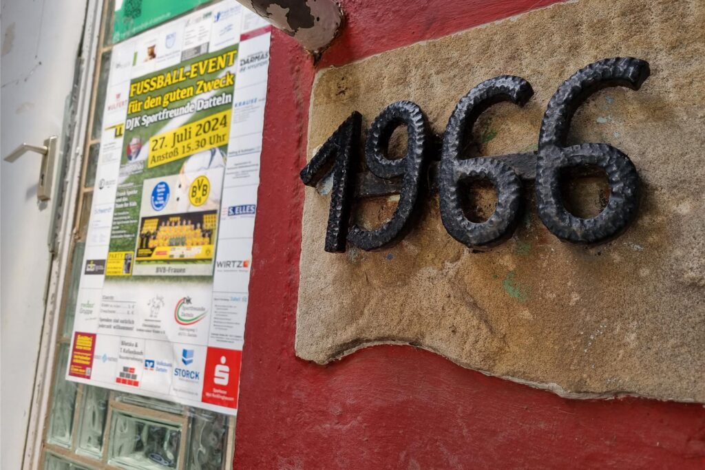Die Zahl 1966 hängt an einer Hauswand. Daneben hängt ein Plakat. 