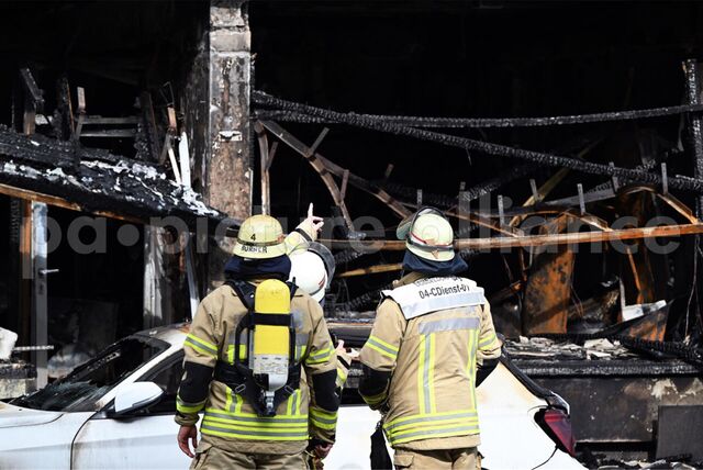Einsatzkräfte der Feuerwehr stehen vor einem Wohnhaus, in dem ein Brand wütete.