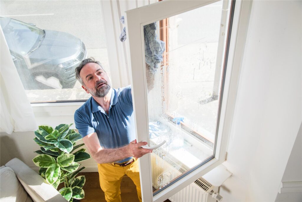 Ein Mann putzt die Fenster seiner Wohnung. An viel befahrenen Straßen sind die Fensterscheiben schneller verschmutzt.