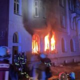 Feuerwehrleute gehen in ein brennendes Haus. Die Flammen schlagen aus den Fenstern der Erdgeschosswohnung.