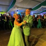 Ein Schütze und eine Frau im Abendkleid tanzen, im Hintergrund sind weitere festlich gekleidete Menschen zu sehen.
