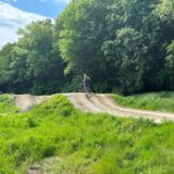 Inmitten einer grünen Wiese ist eine Mountainbike-Strecke aus Hügeln. Ein Fahrradfahrer ist mitten im Sprung auf dem Hügel in der Mitte des Bildes.