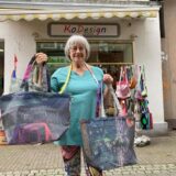 Kornelia Helisch zeigt vor ihrem Geschäft KoDesign am Holzmarkt in Recklinghausen einige restliche Exemplare von Einkaufstaschen, die aus einer Baustellenplane genäht sind, die etwa vier Jahre am Stadthaus E gehangen hatte.