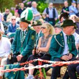 Männer in Schützenuniform und Besucher in „Zivil“ sitzen im Freien auf Bänken und halten Bierflaschen in der Hand.